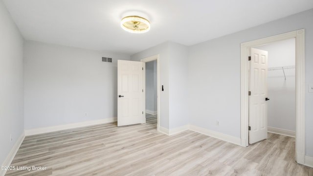 unfurnished bedroom with a walk in closet, light hardwood / wood-style flooring, and a closet