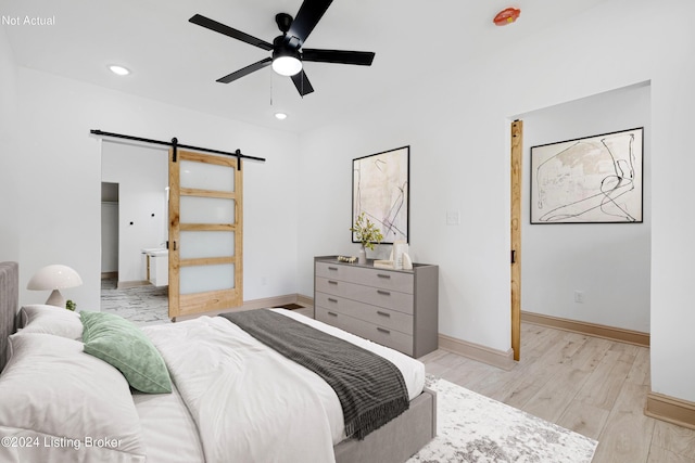 bedroom with ceiling fan, a barn door, and light wood-type flooring