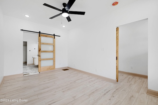 unfurnished room featuring ceiling fan, a barn door, and light wood-type flooring