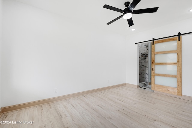 empty room featuring ceiling fan, a barn door, and light hardwood / wood-style flooring