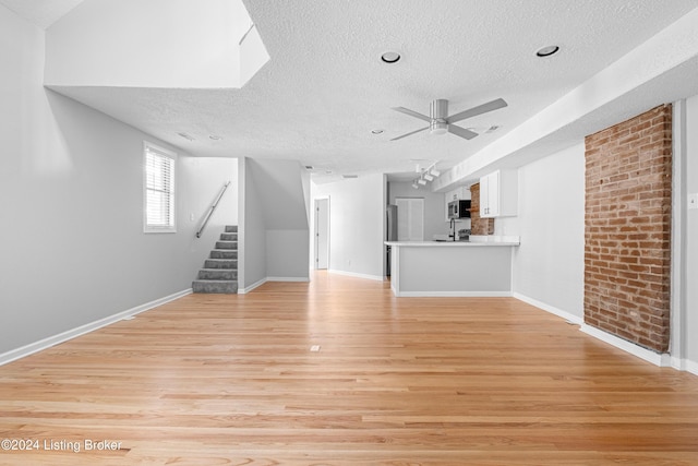 unfurnished living room with ceiling fan, light wood-type flooring, and a textured ceiling