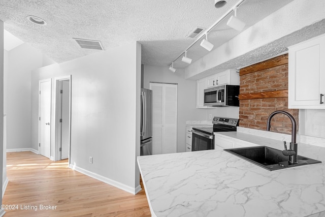 kitchen featuring sink, stainless steel appliances, a textured ceiling, white cabinets, and light wood-type flooring