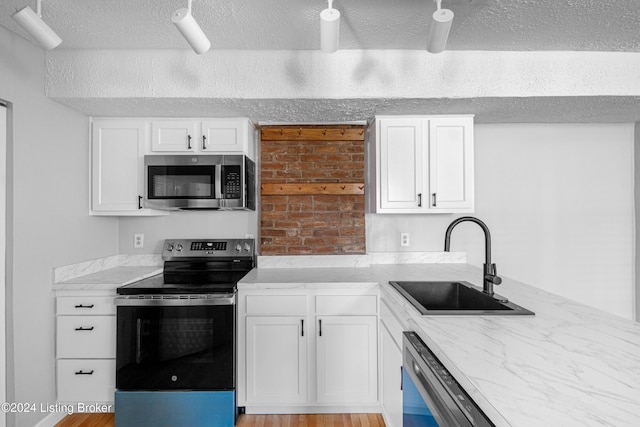 kitchen with sink, a textured ceiling, appliances with stainless steel finishes, light hardwood / wood-style floors, and white cabinetry