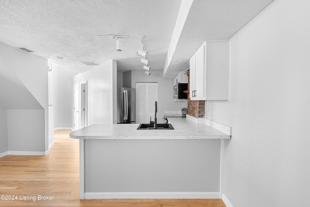 kitchen with sink, rail lighting, stainless steel appliances, kitchen peninsula, and white cabinets