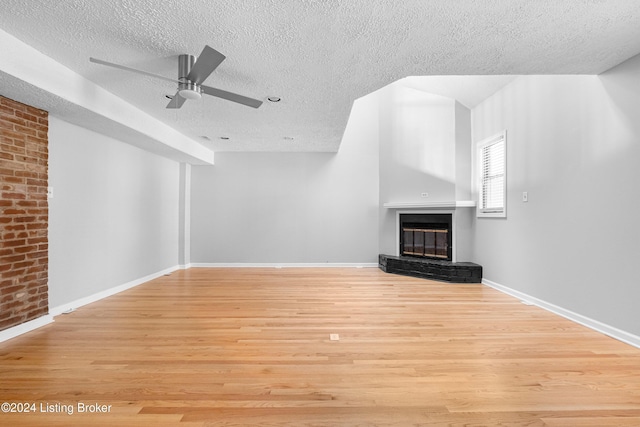 unfurnished living room featuring a textured ceiling, a large fireplace, light hardwood / wood-style flooring, and ceiling fan