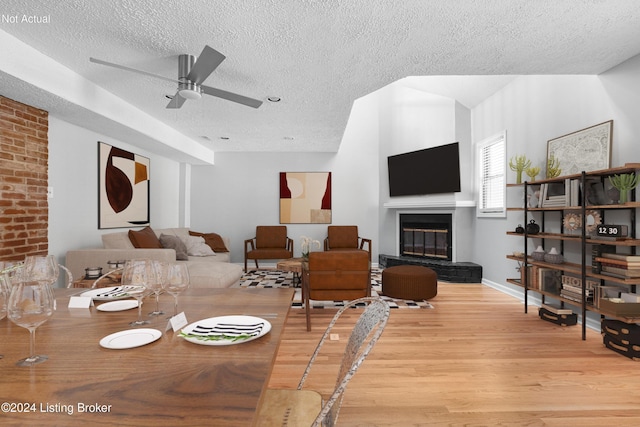 dining area featuring ceiling fan, a large fireplace, light hardwood / wood-style floors, and a textured ceiling