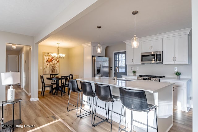 kitchen with a kitchen island with sink, sink, appliances with stainless steel finishes, decorative light fixtures, and white cabinetry