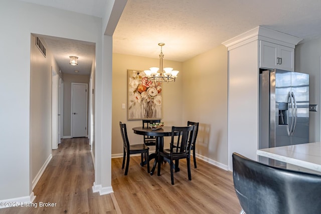 dining room featuring light hardwood / wood-style floors, a textured ceiling, and an inviting chandelier