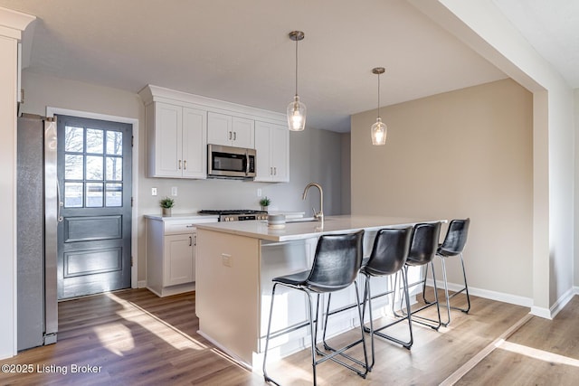 kitchen featuring stainless steel appliances, light hardwood / wood-style flooring, pendant lighting, a center island with sink, and white cabinets