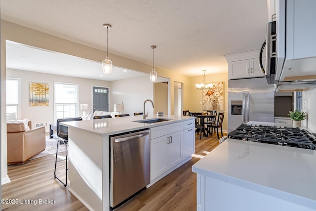 kitchen with sink, stainless steel appliances, decorative light fixtures, a center island with sink, and white cabinets