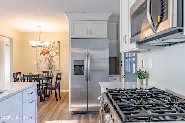 kitchen with light wood-type flooring, light stone counters, stainless steel appliances, a notable chandelier, and white cabinetry