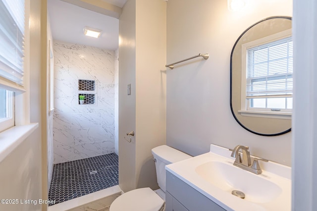 bathroom with a tile shower, vanity, and toilet