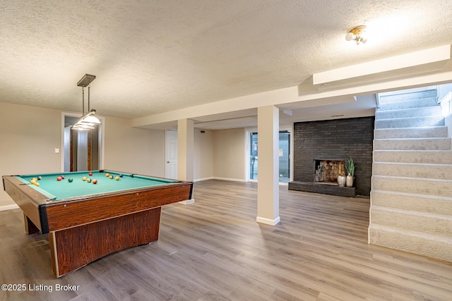 playroom featuring hardwood / wood-style floors, a textured ceiling, a brick fireplace, and billiards