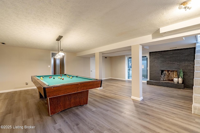 recreation room with wood-type flooring, a textured ceiling, pool table, and a brick fireplace