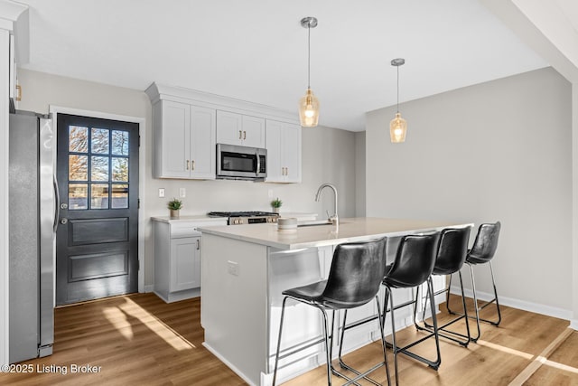 kitchen with white cabinetry, hanging light fixtures, an island with sink, appliances with stainless steel finishes, and light wood-type flooring