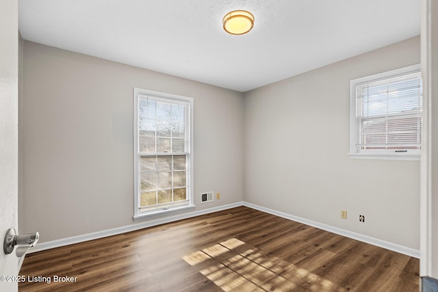 empty room with dark hardwood / wood-style flooring and plenty of natural light