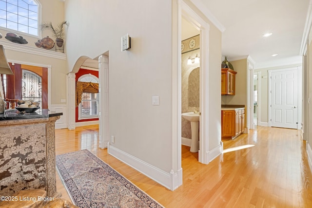 hall with ornate columns, ornamental molding, and light hardwood / wood-style flooring