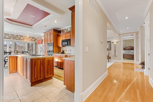 kitchen featuring a raised ceiling, a center island with sink, light tile patterned floors, and ornamental molding