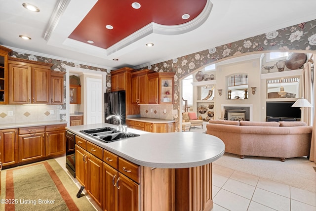 kitchen with a tray ceiling, crown molding, sink, black appliances, and a center island with sink