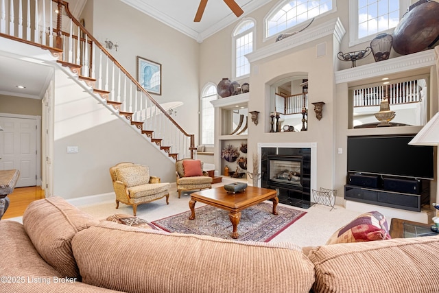 living room with ceiling fan, a tile fireplace, crown molding, and a high ceiling