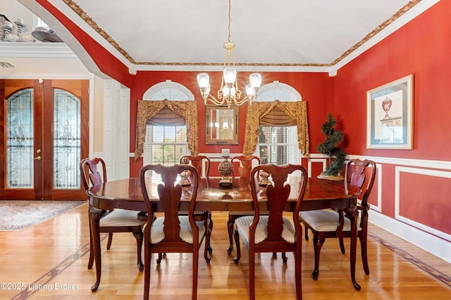 dining space with a chandelier, french doors, crown molding, and wood-type flooring