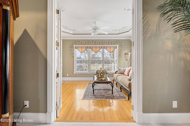 sitting room with hardwood / wood-style floors, ceiling fan, a raised ceiling, and crown molding