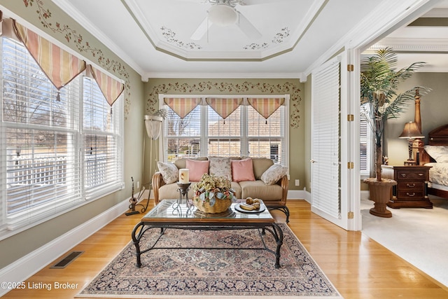 living room with ceiling fan, ornamental molding, light hardwood / wood-style flooring, and a tray ceiling