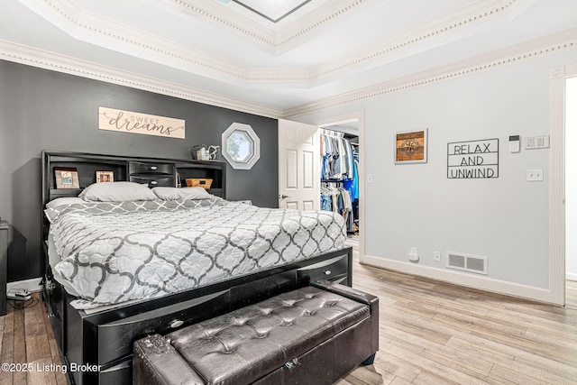 bedroom featuring a walk in closet, hardwood / wood-style flooring, a raised ceiling, and a closet