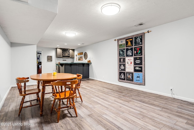 dining space with bar area, a textured ceiling, and light hardwood / wood-style flooring