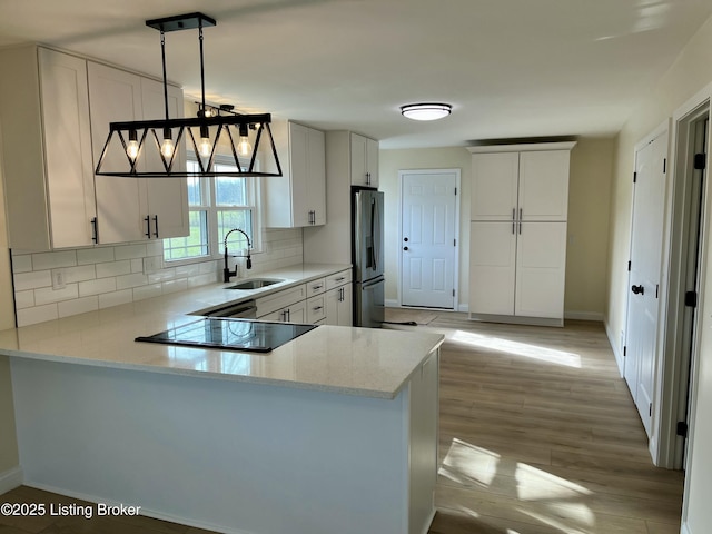 kitchen with kitchen peninsula, backsplash, sink, stainless steel fridge with ice dispenser, and hanging light fixtures