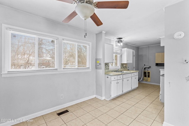 kitchen featuring decorative backsplash, white cabinets, light tile patterned flooring, ceiling fan, and sink