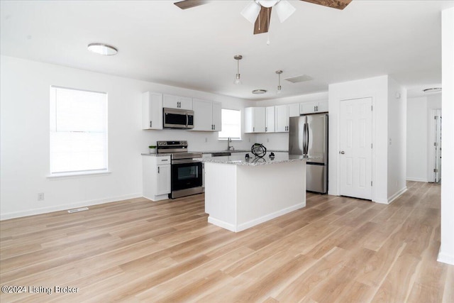 kitchen with white cabinets, appliances with stainless steel finishes, decorative light fixtures, a kitchen island, and light stone counters