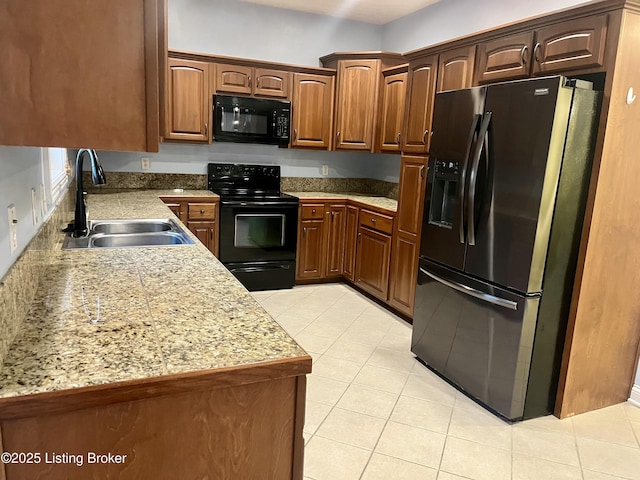 kitchen with light stone countertops, sink, light tile patterned floors, and black appliances