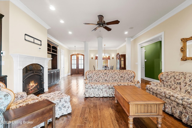 living room with ornate columns, dark hardwood / wood-style flooring, ceiling fan with notable chandelier, and ornamental molding