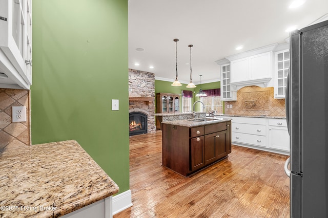 kitchen featuring sink, decorative light fixtures, a center island with sink, a fireplace, and stainless steel refrigerator