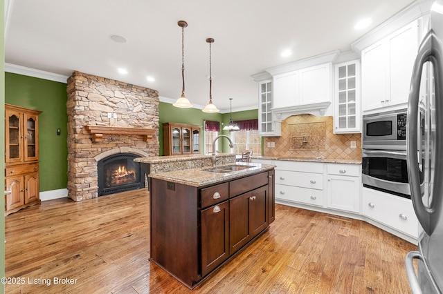 kitchen featuring stainless steel appliances, sink, a center island with sink, a stone fireplace, and hanging light fixtures