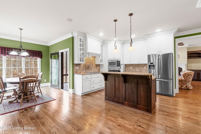 kitchen with appliances with stainless steel finishes, backsplash, light stone counters, a notable chandelier, and white cabinetry