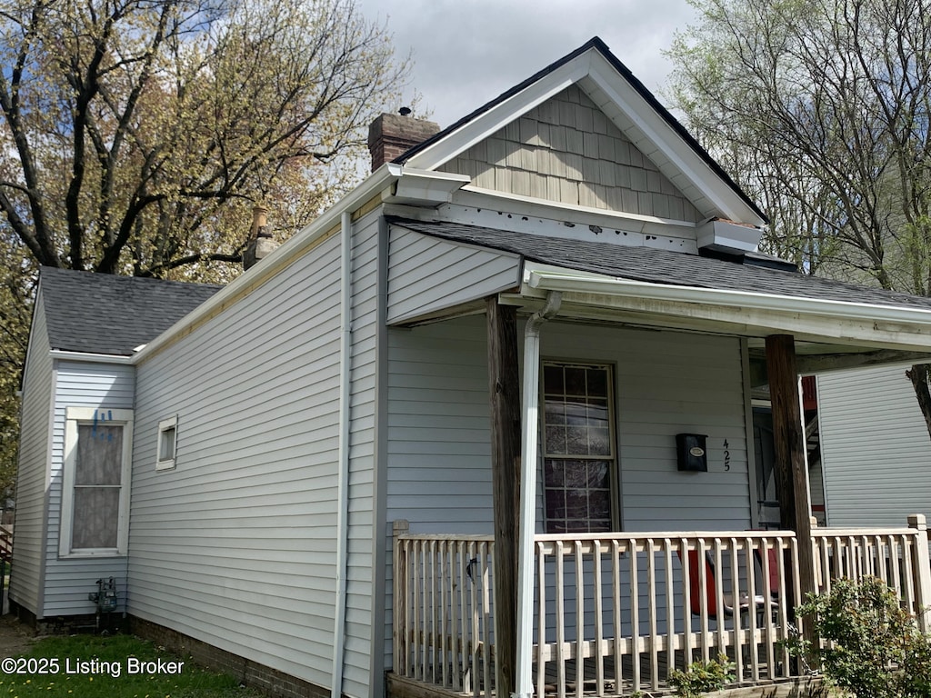 view of side of home featuring roof with shingles and a porch