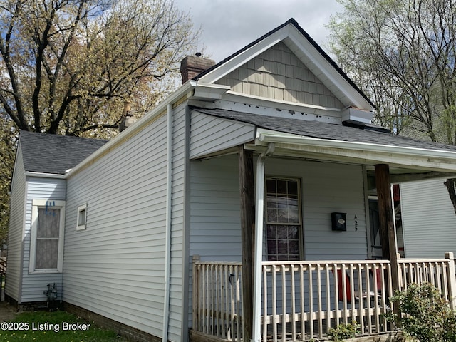 view of side of home featuring roof with shingles and a porch