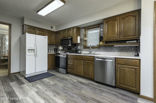 kitchen featuring sink, stainless steel appliances, tasteful backsplash, light hardwood / wood-style floors, and a textured ceiling