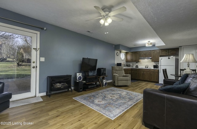 living room with a textured ceiling, light hardwood / wood-style floors, and ceiling fan