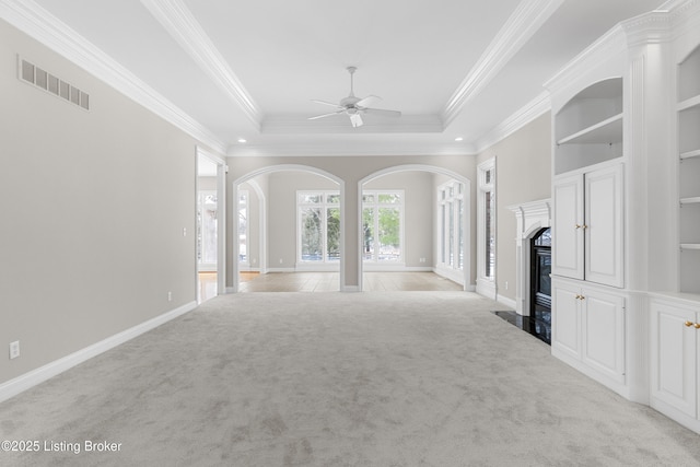 unfurnished living room with a high end fireplace, a tray ceiling, crown molding, and light colored carpet