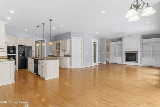 kitchen featuring black appliances, ceiling fan with notable chandelier, a center island with sink, hanging light fixtures, and built in features