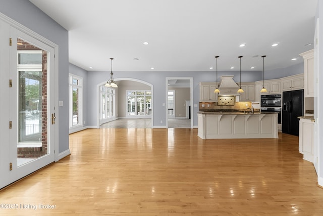 kitchen featuring a breakfast bar, a center island, black appliances, decorative light fixtures, and light hardwood / wood-style floors