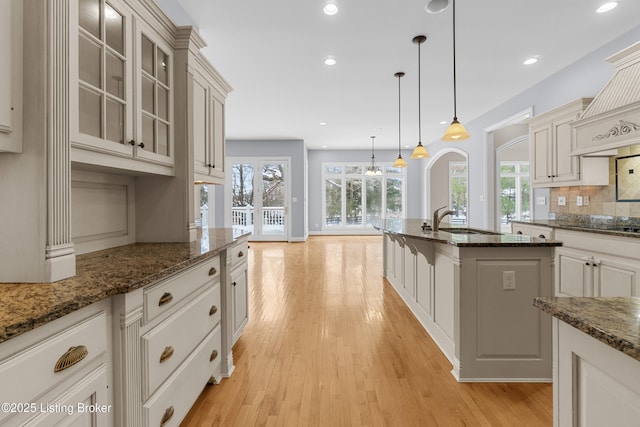 kitchen with backsplash, dark stone counters, sink, decorative light fixtures, and light hardwood / wood-style floors