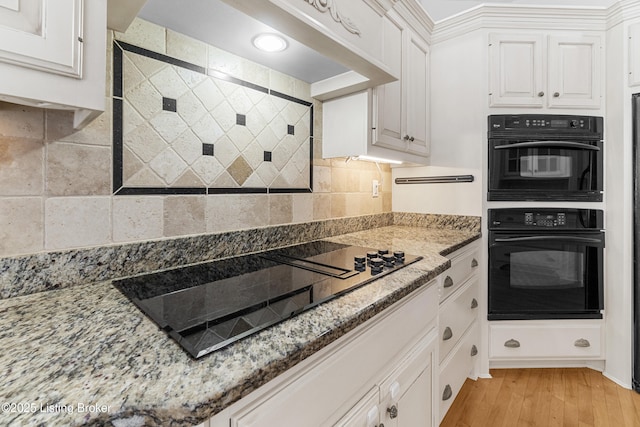 kitchen featuring light stone countertops, light wood-type flooring, white cabinetry, and black appliances