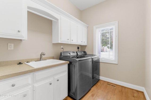 clothes washing area with light hardwood / wood-style floors, cabinets, sink, and washing machine and clothes dryer