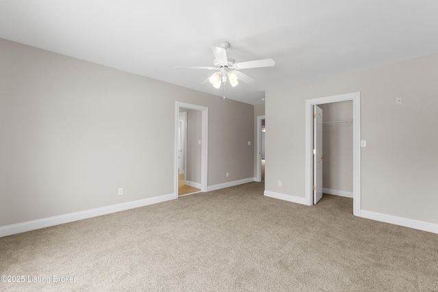 unfurnished bedroom featuring light carpet, a walk in closet, a closet, and ceiling fan