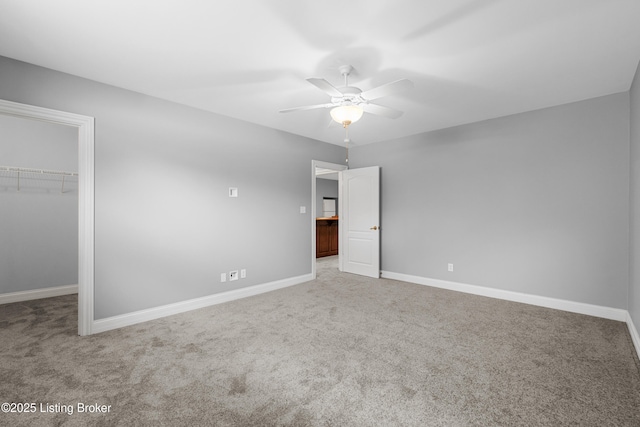 unfurnished bedroom with a walk in closet, a closet, ceiling fan, and carpet floors