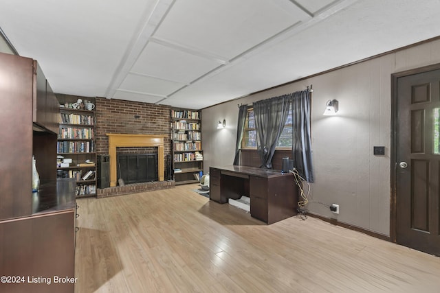 unfurnished office with wood walls, built in shelves, light hardwood / wood-style floors, and a brick fireplace